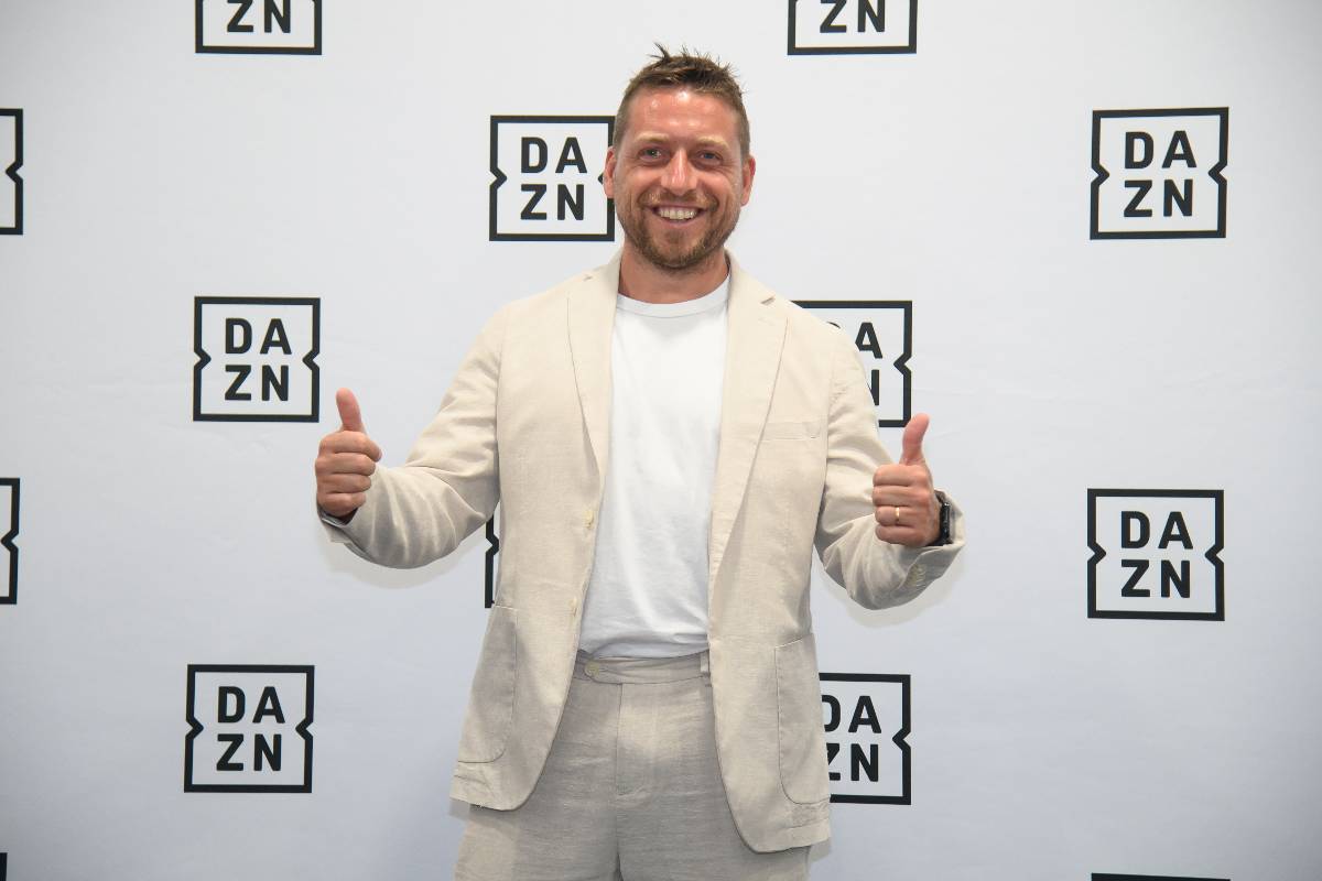 Emanuele Giaccherini posa sorridente davanti al backdrop DAZN, vestito in abito chiaro durante un evento ufficiale dell’emittente sportiva.