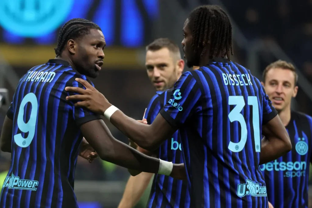 Giocatori dell'Inter in maglia a strisce blu e nera si intrattengono durante una partita, con focus su due calciatori che conversano in campo