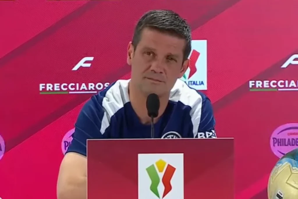 Chivu durante una conferenza stampa con microfono, indossa la tuta azzurra della nazionale italiana