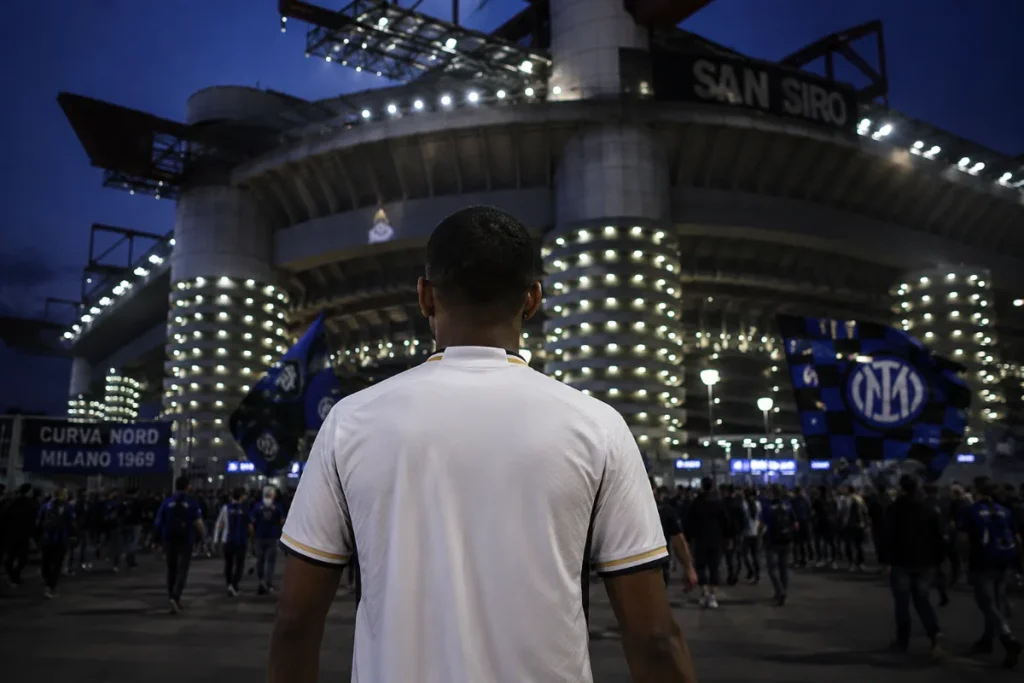 Giocatore in maglia bianca davanti a San Siro di notte, stadio illuminato