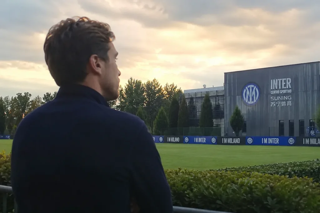 Uomo di spalle osserva il campo di allenamento dell'Inter con centro sportivo Suning sullo sfondo