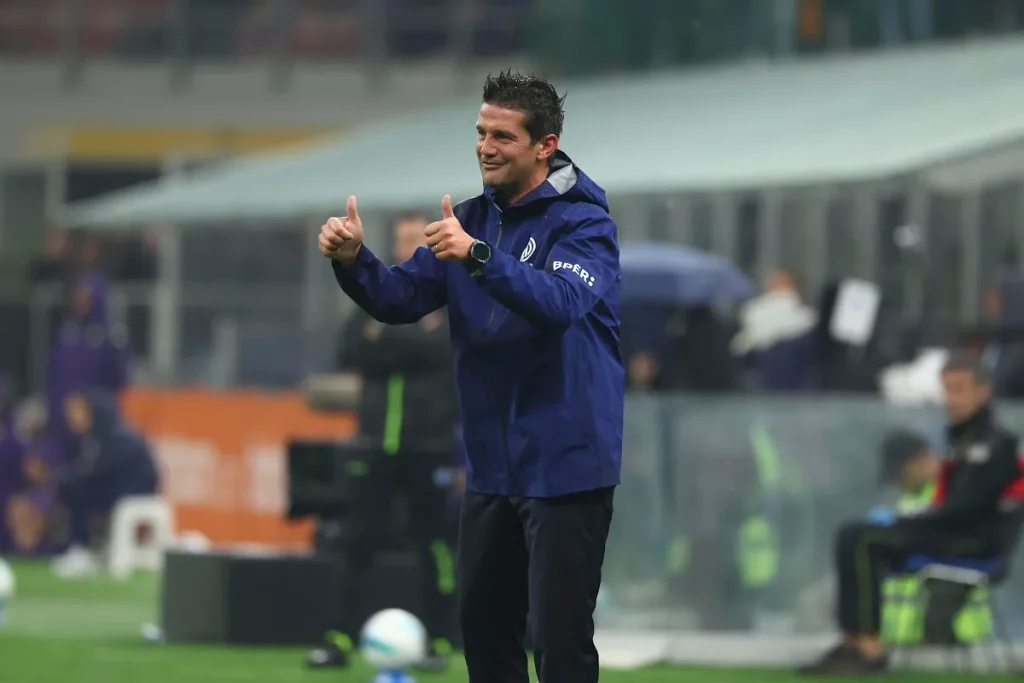 Chivu sorride e fa il gesto del pollice in su durante una partita, indossa la giacca tecnica blu della Juventus in panchina