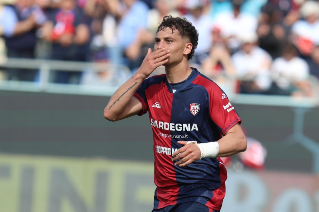 Sebastiano Esposito durante una partita con la maglia del Cagliari, mano alla bocca in espressione di concentrazione