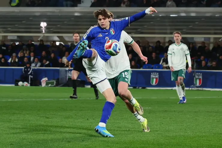 Giovane calciatore in maglia azzurra dell'Italia controlla il pallone durante una partita in stadio