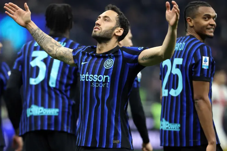 Calhanoglu con le braccia alzate indossa la maglia dell'Inter a righe blu e nero durante una partita