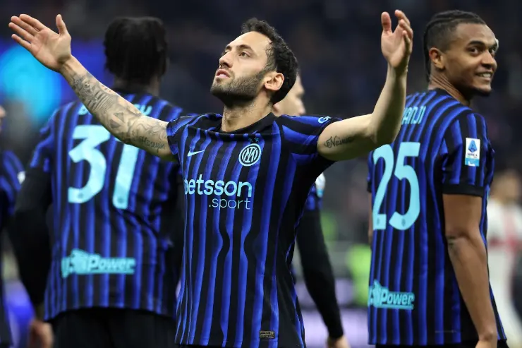 Calhanoglu con le braccia alzate indossa la maglia dell'Inter a strisce blu e nerazzurre con sponsor Betsson