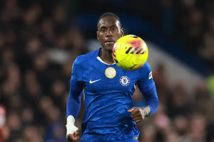 Calciatore in maglia Chelsea durante una partita, con il pallone giallo in primo piano.