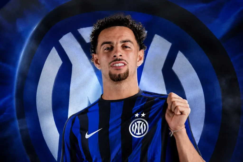 Curtis Jones in maglia Inter a strisce blu e nere sorride davanti allo stemma nerazzurro