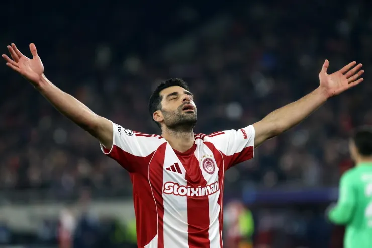 Mehdi Taremi esulta con le braccia alzate indossando la maglia del Olympiacos a strisce rosse e bianche