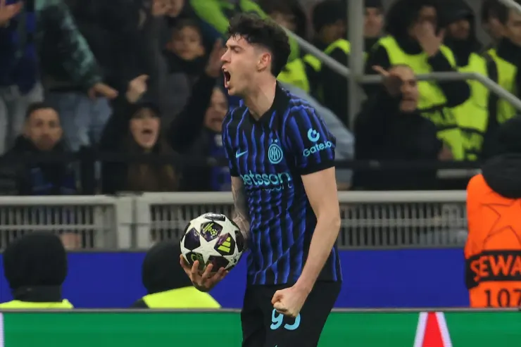 Bastoni in maglia Inter a righe blu e nere esulta in campo con il pallone in mano