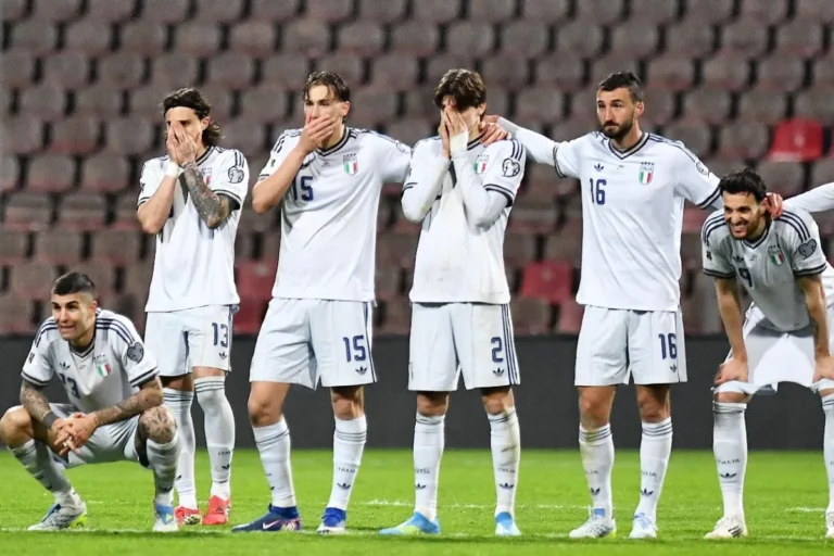 Giocatori della Nazionale italiana in uniforme bianca con espressioni concentrate durante una partita, alcuni con le mani al volto
