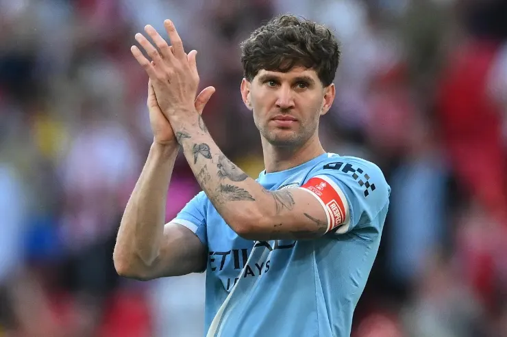 John Stones in maglia azzurra applaude verso il pubblico dello stadio, con fascia da capitano visibile al braccio