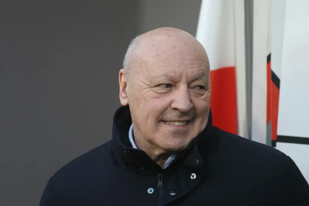 Beppe Marotta, dirigente Inter, sorride durante un evento ufficiale con lo stemma dell'Inter visibile sullo sfondo