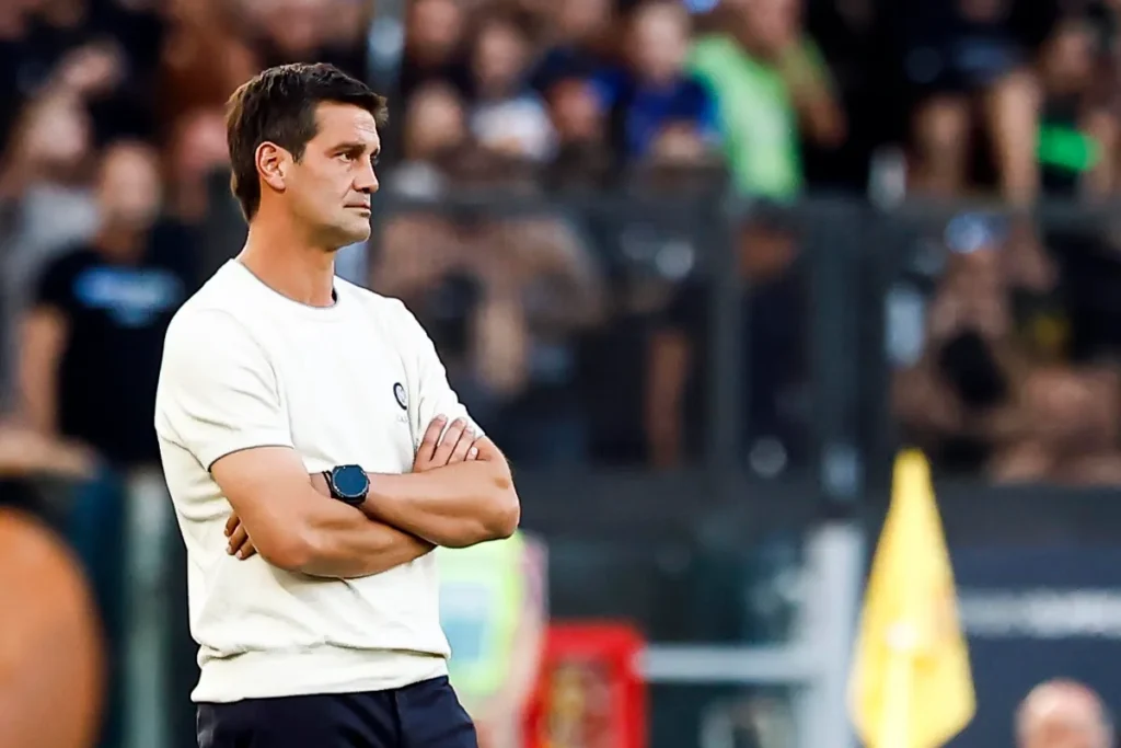 Chivu durante una partita, con le braccia incrociate in panchina, sullo sfondo il pubblico dello stadio