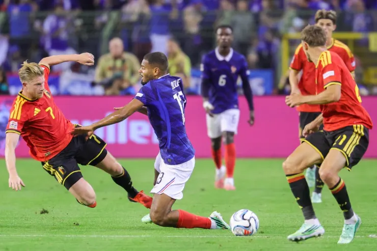De Bruyne in maglia blu contrasta con giocatore in rosso durante partita internazionale di calcio