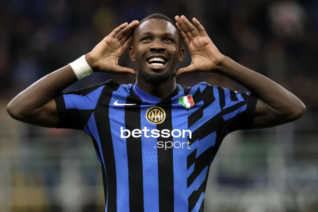 Marcus Thuram esulta con le mani ai lati della testa indossando la maglia dell'Inter a righe blu e nere
