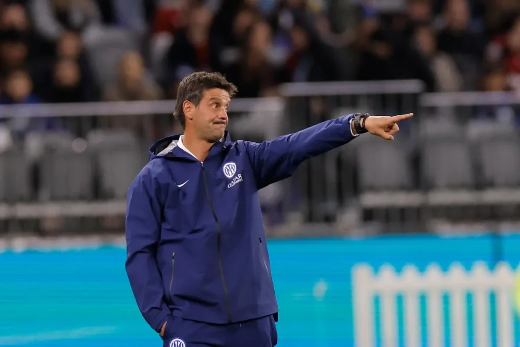 Chivu in tuta blu Nike con logo Iqoniq durante una partita, rivolto verso il campo con gesto di indicazione