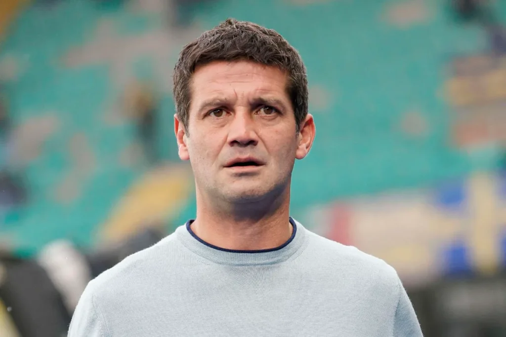 Chivu in maglia grigio chiaro e colletto blu sullo sfondo di uno stadio sfocato