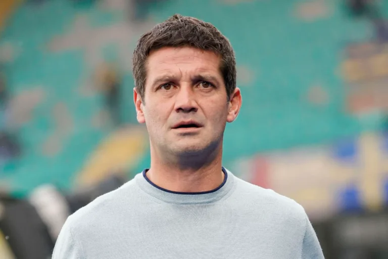 Chivu in maglia grigio chiaro e colletto blu sullo sfondo di uno stadio sfocato