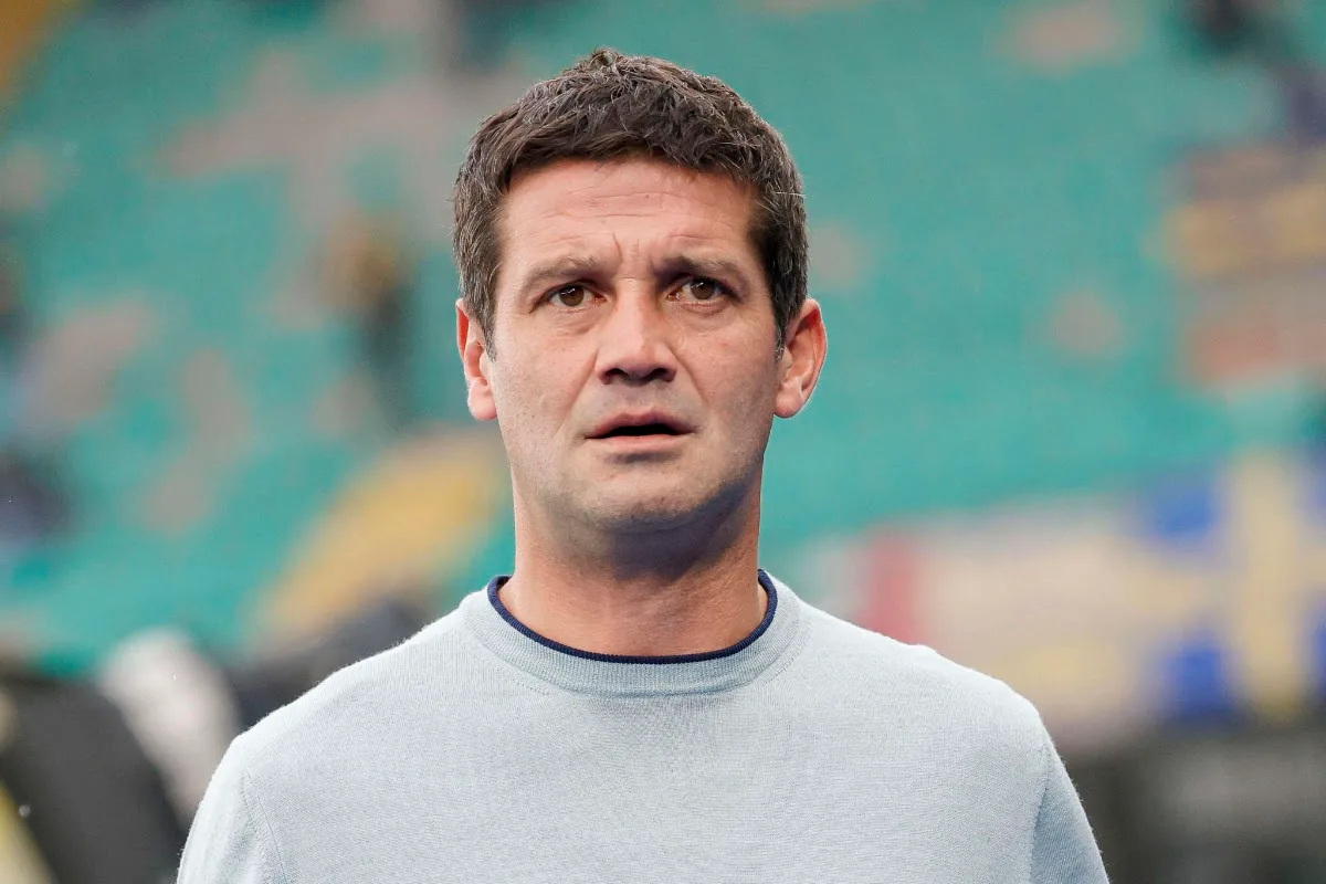 Chivu in maglia grigio chiaro e colletto blu sullo sfondo di uno stadio sfocato