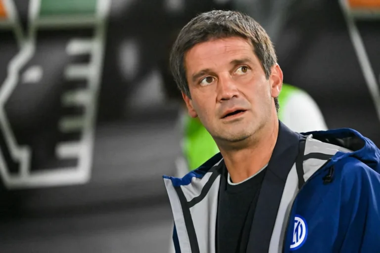 Uomo con giacca blu dell'Inter e stemma, in panchina allo stadio, con lo sguardo rivolto verso l'alto