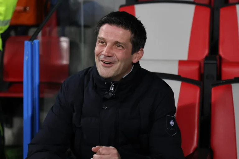 Cristian Chivu sorride dalla panchina dell'Inter durante una partita, indossando la giacca tecnica del club