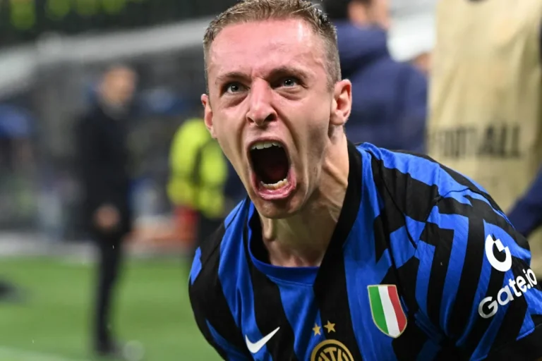 Giocatore dell'Inter con maglia nerazzurra esulta urlando a bocca aperta, con sfondo sfocato da stadio