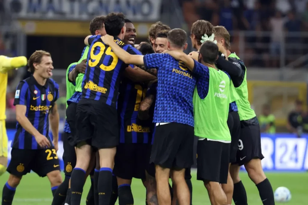 Giocatori dell'Inter abbracciati in un'esultanza di gruppo in campo, con maglie a righe nerazzurre e sponsor Betsson e Upower