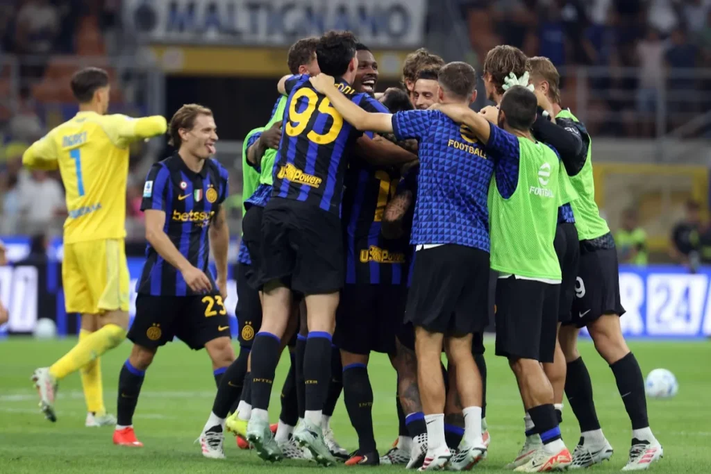Giocatori dell'Inter esultano abbracciati in cerchio sul prato, con maglie nerazzurre a strisce e pettorine verdi dello staff