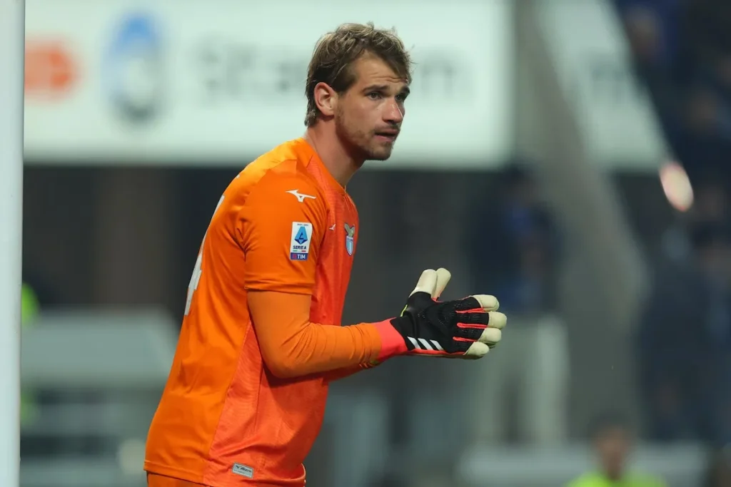Portiere con maglia arancione Mizuno e stemma Lazio, patch Serie A TIM e guanti neri e bianchi durante una partita
