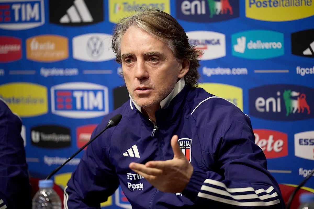 Mancini in conferenza stampa con la giacca blu della Nazionale italiana con stemma FIGC, davanti ai loghi degli sponsor