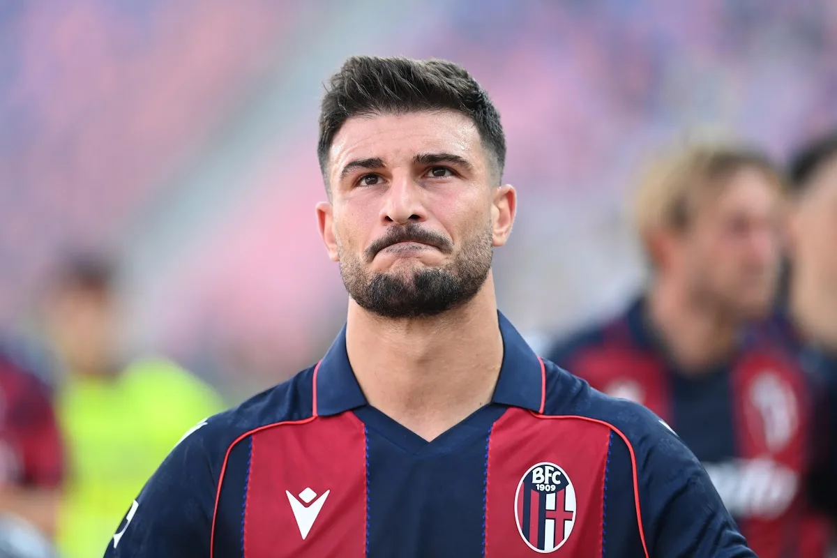 Orsolini del Bologna con maglia rossoblù e stemma BFC 1909, in primo piano con sguardo serio durante una partita